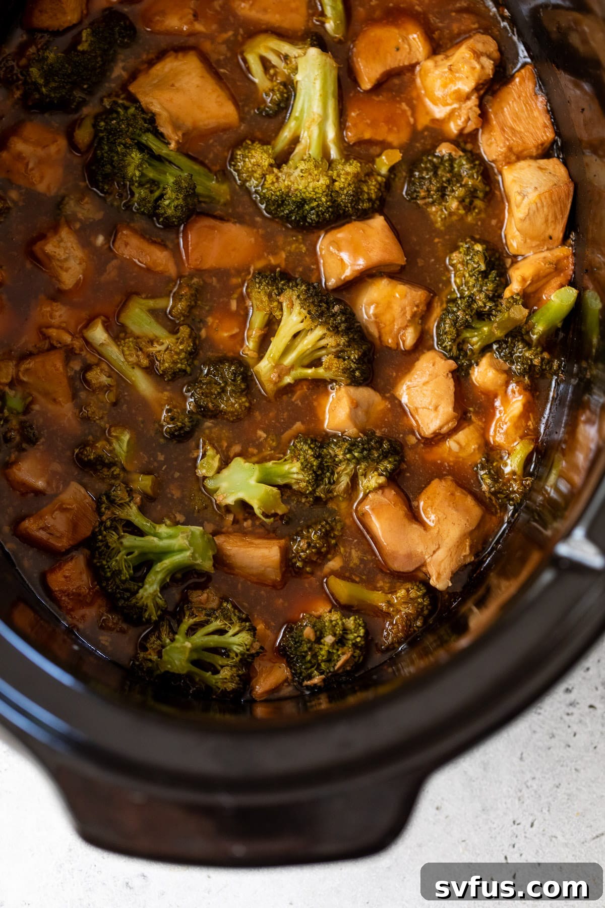 Close-up of cooked broccoli florets and chicken pieces in thick orange sauce in a slow cooker, ready to be served.