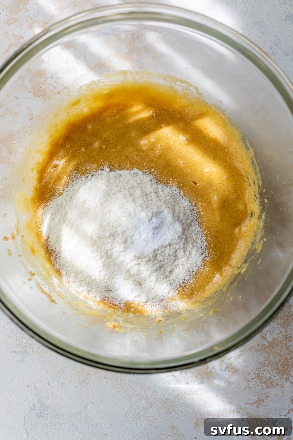 Dry ingredients layered on top of the wet coconut flour cookie batter in a large glass bowl, ready to be mixed.