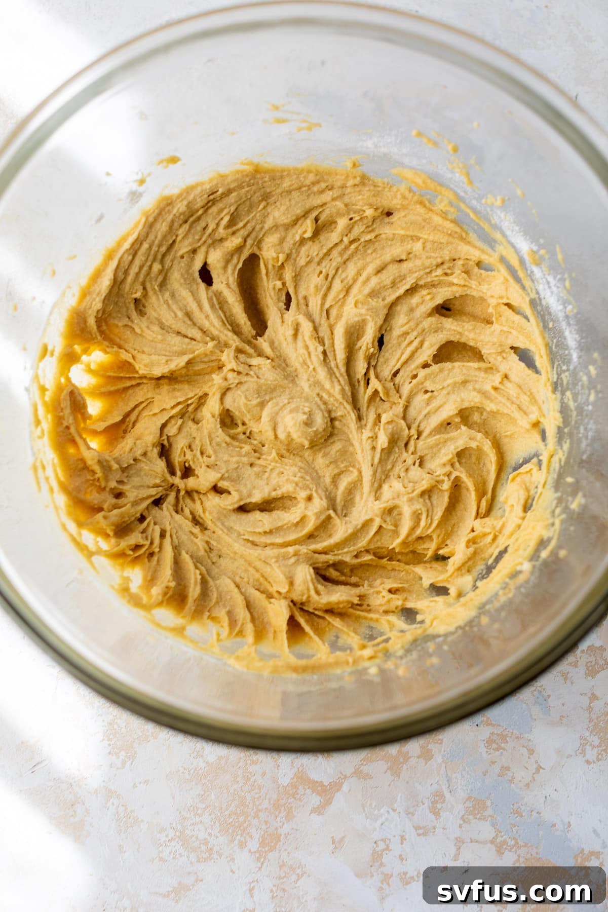 Smooth, light brown coconut flour cookie dough in a large glass bowl after all ingredients have been mixed.