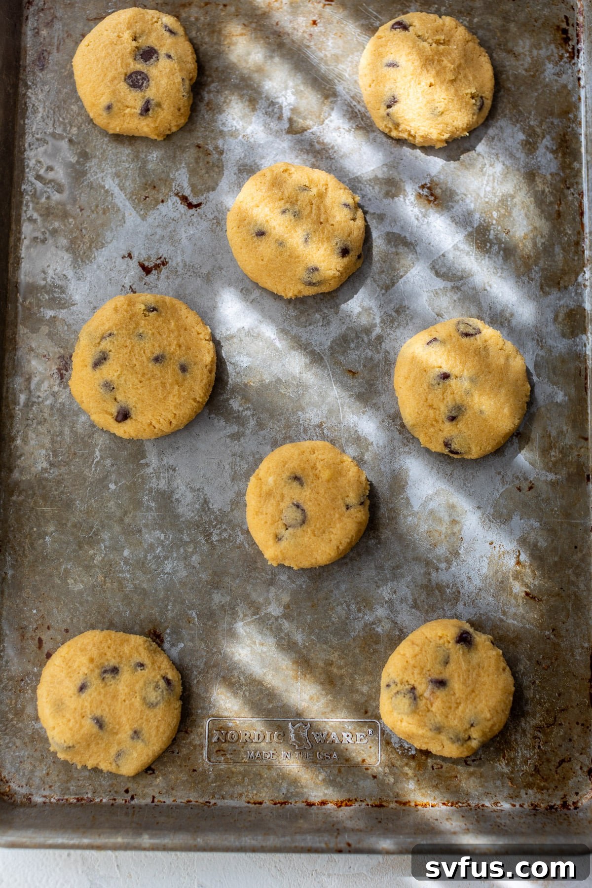 Unbaked coconut flour cookies, shaped and flattened, on a metal baking sheet, ready for the oven.