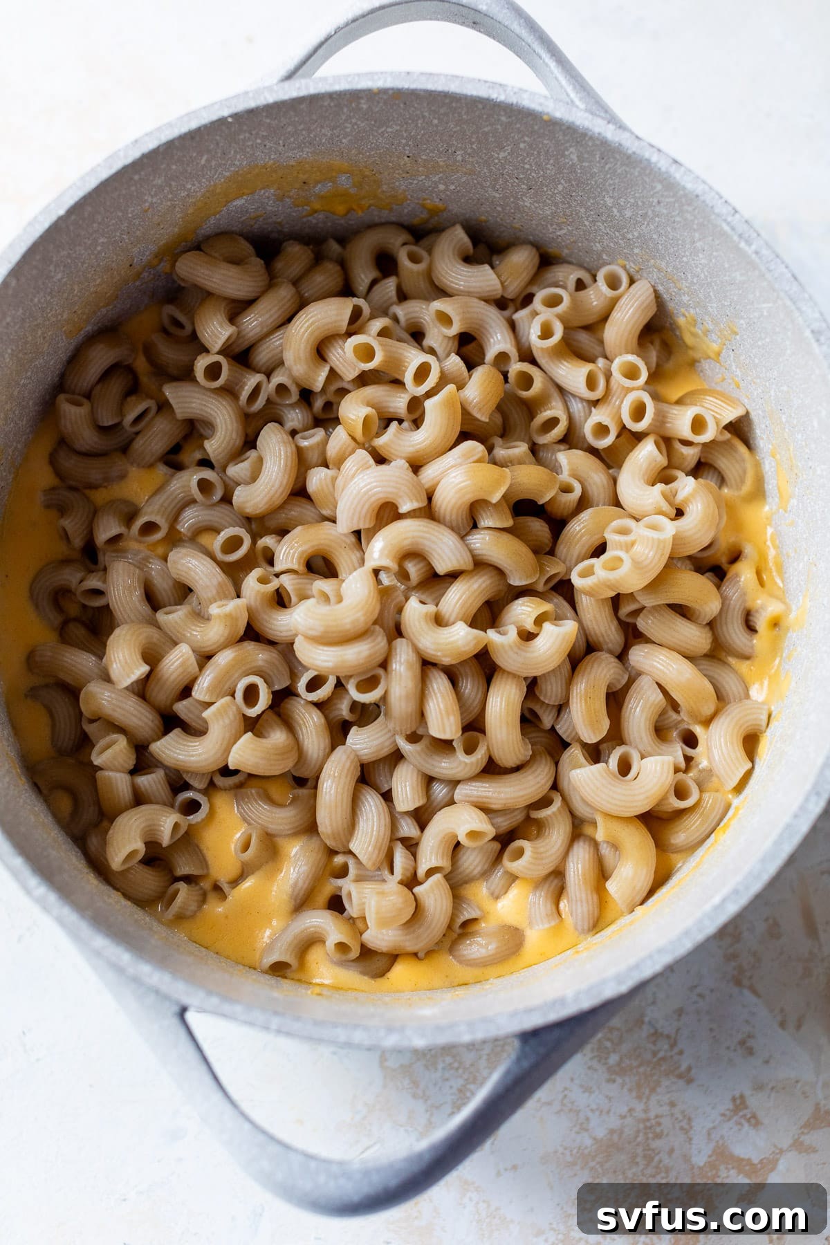 cooked macaroni noodles gently stirred into a large pot of cottage cheese mac and cheese sauce.