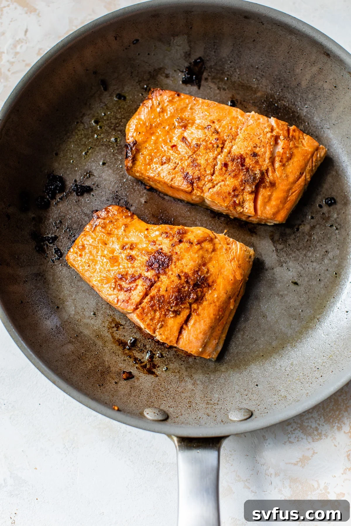 Cooked salmon fillets with crispy skin searing in a hot skillet, surrounded by a light sizzle.