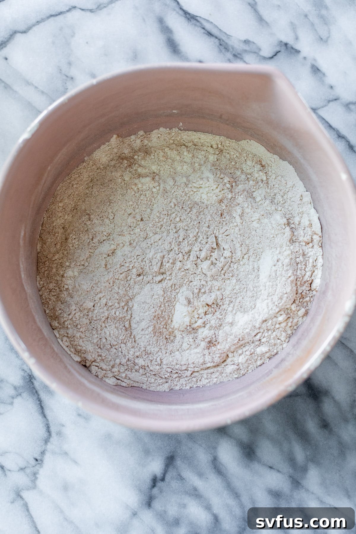 The dry ingredients for apple oatmeal cookies, including flour, cinnamon, baking soda, baking powder, and salt, are perfectly mixed together in a pink bowl.