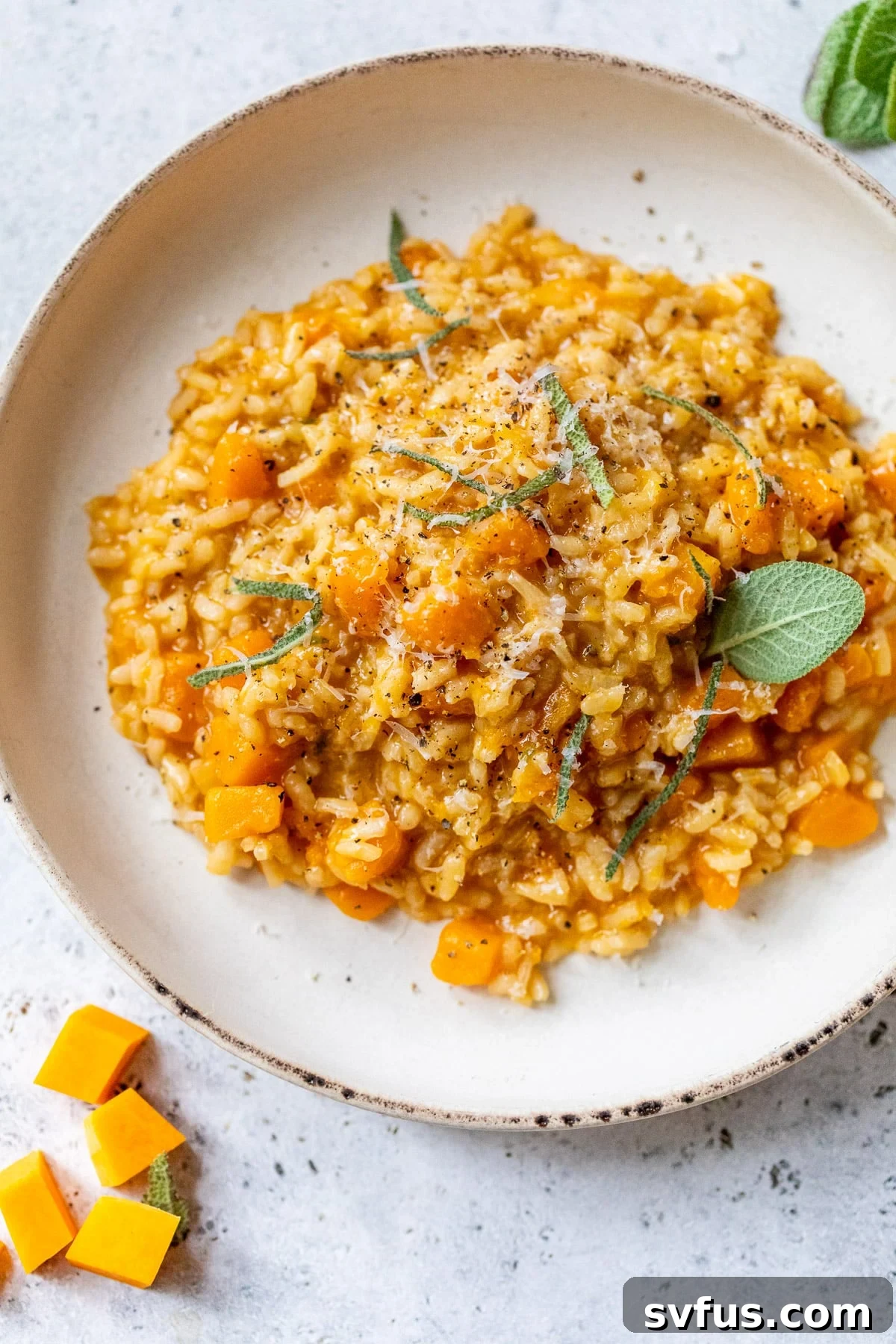 A vibrant plate of creamy Butternut Squash Risotto, beautifully garnished with fresh sage leaves and a generous sprinkle of grated Parmesan cheese, highlighting its rich autumn colors and inviting texture.