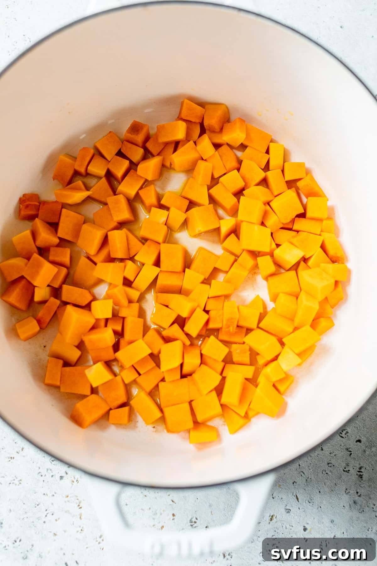 Diced butternut squash and aromatic vegetables like shallots and garlic being sautéed in a large pot, an essential initial step for the risotto.