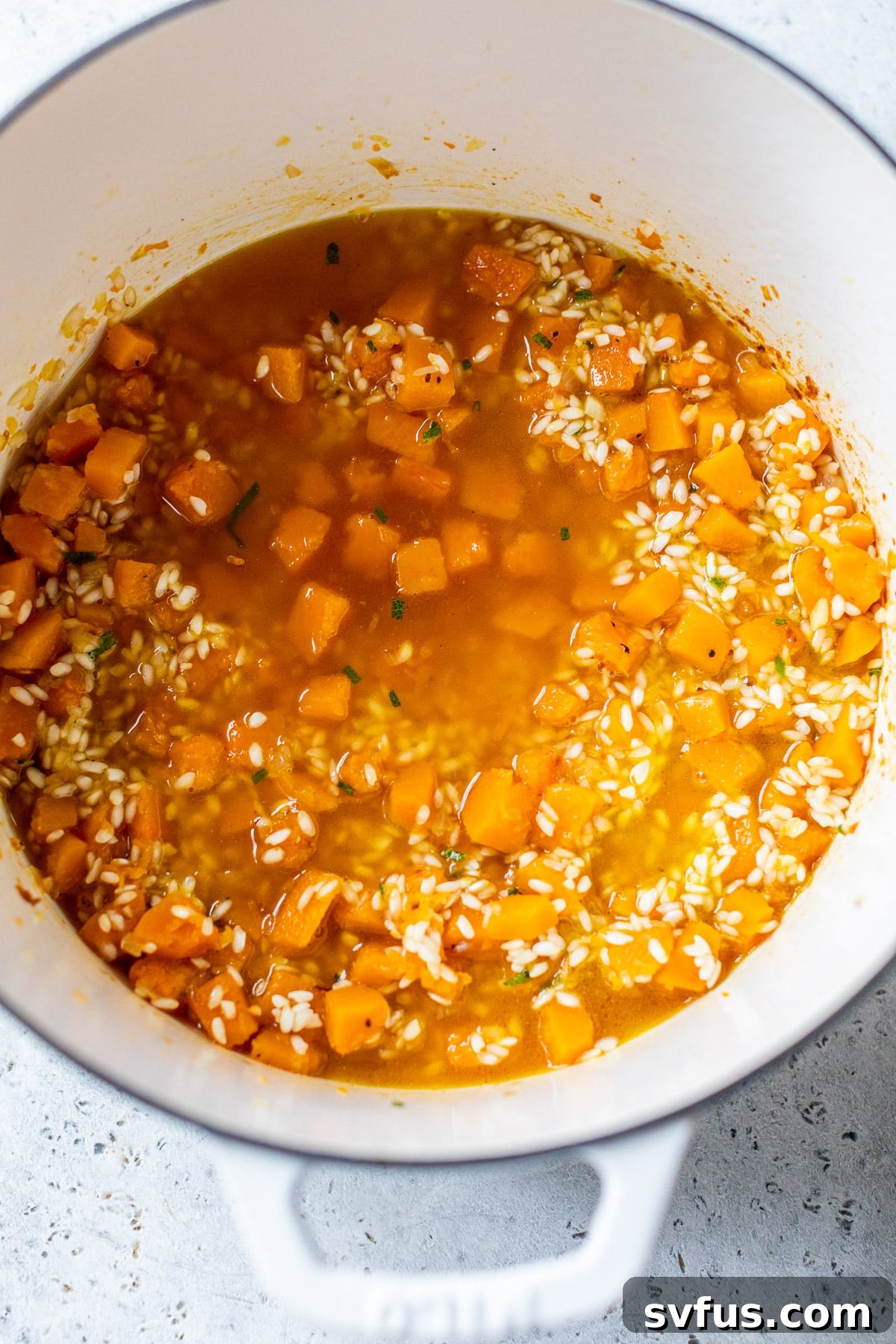 Close-up view of creamy risotto with butternut squash and broth in a large pot, showcasing the rich texture and ongoing cooking process.