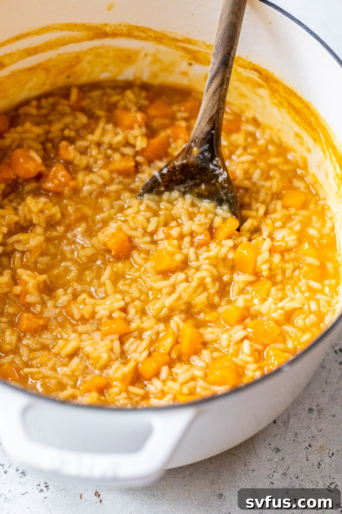 A wooden spoon gently stirring a pot full of rich and creamy butternut squash risotto, illustrating its luscious, ready-to-serve consistency.