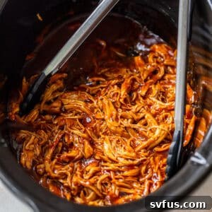 Metal tongs inside a crockpot with shredded BBQ chicken.