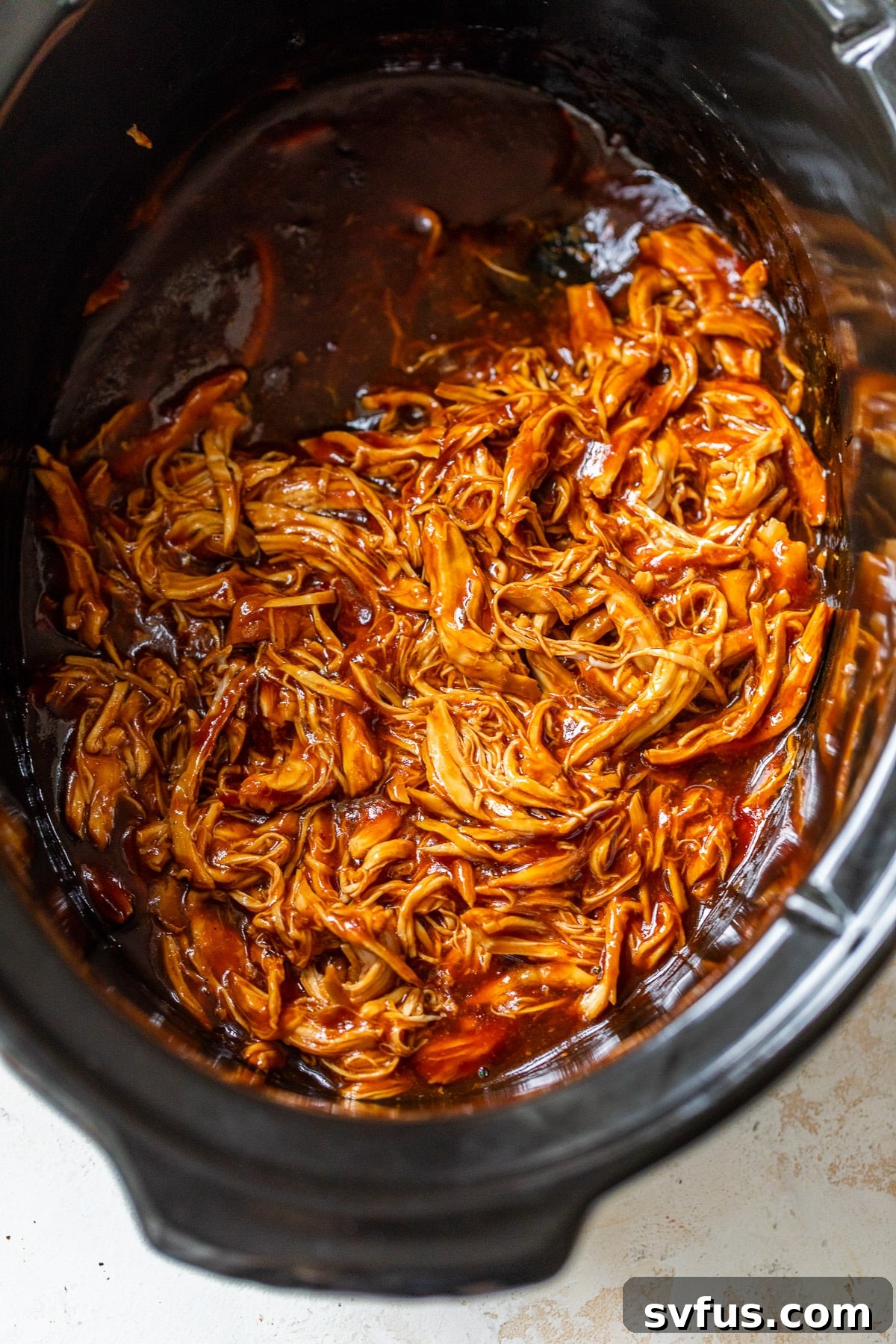 Overhead view of perfectly shredded BBQ chicken simmering in a crockpot, ready to be served.