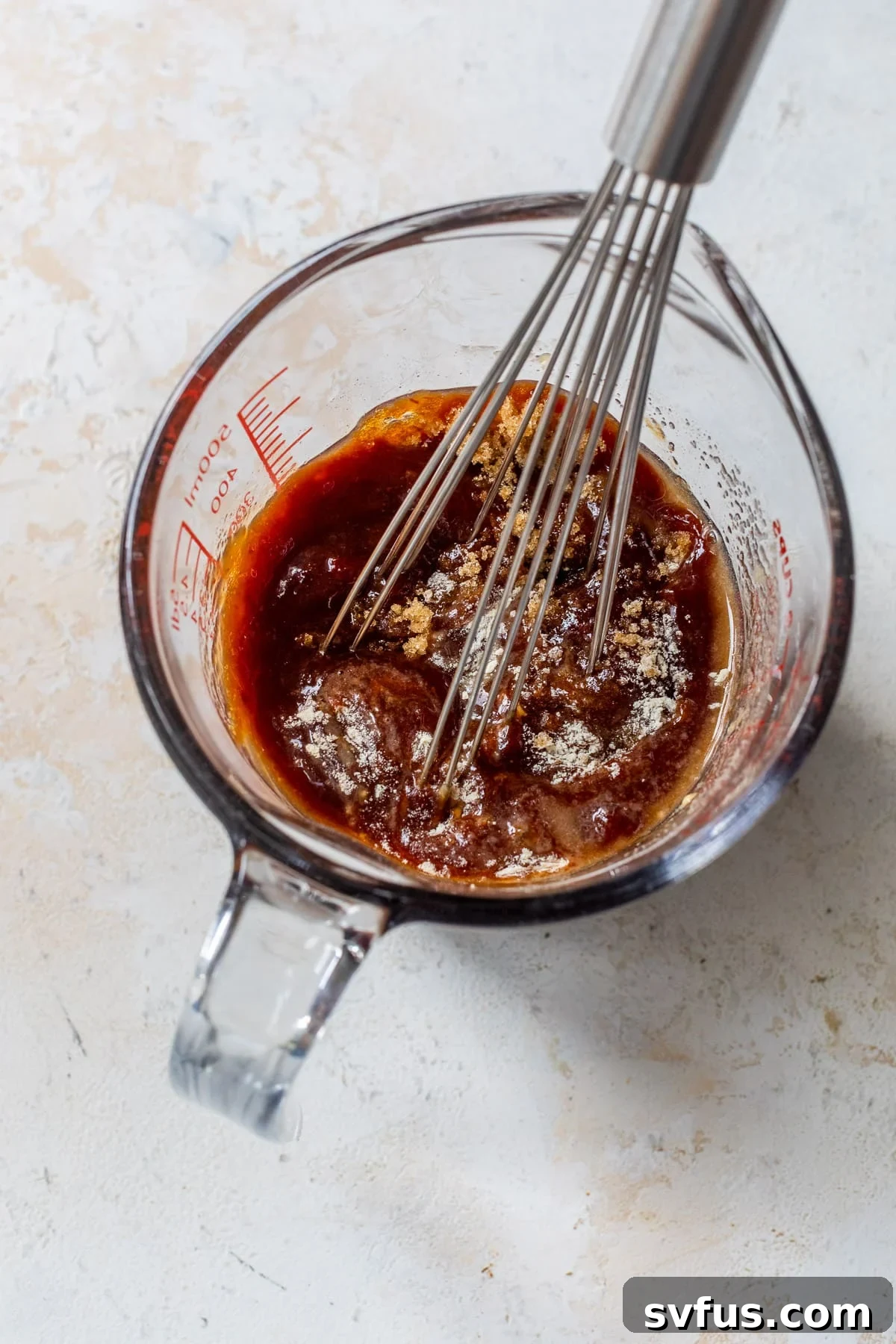 Whisking a seasoned BBQ sauce in a small glass measuring cup, showcasing the smooth consistency before pouring over chicken.