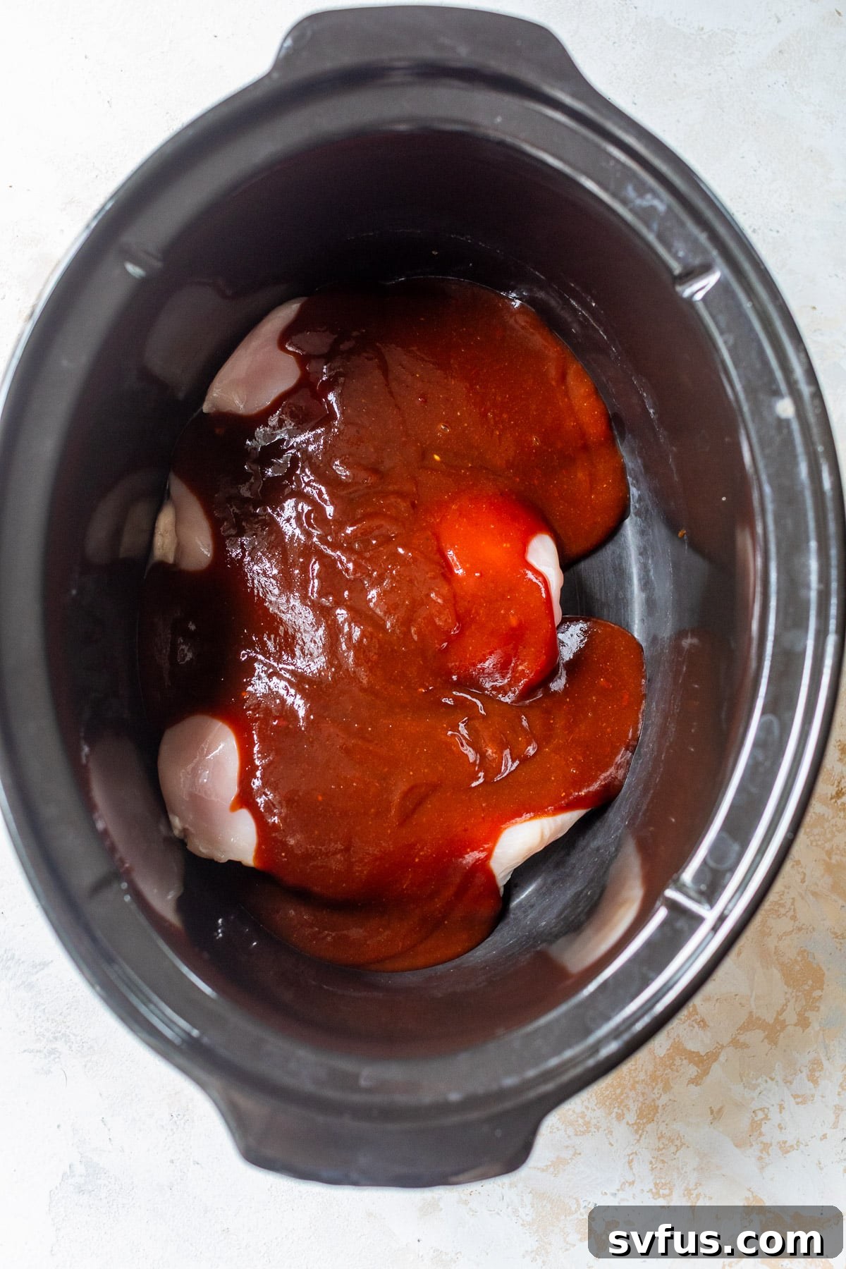Overhead view of raw chicken breasts neatly arranged and covered in BBQ sauce in a crockpot, ready for cooking.