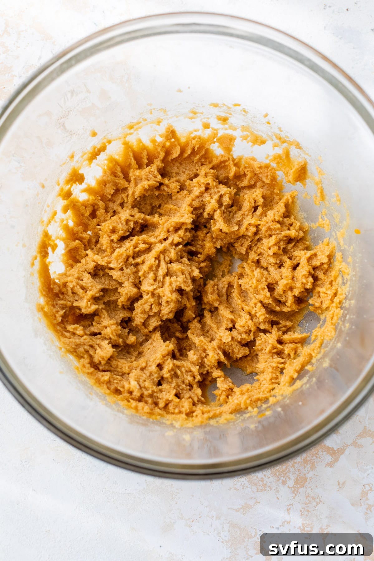 The wet mixed ingredients for Pumpkin Chocolate Chip Cookies in a glass bowl, light orange and fluffy.