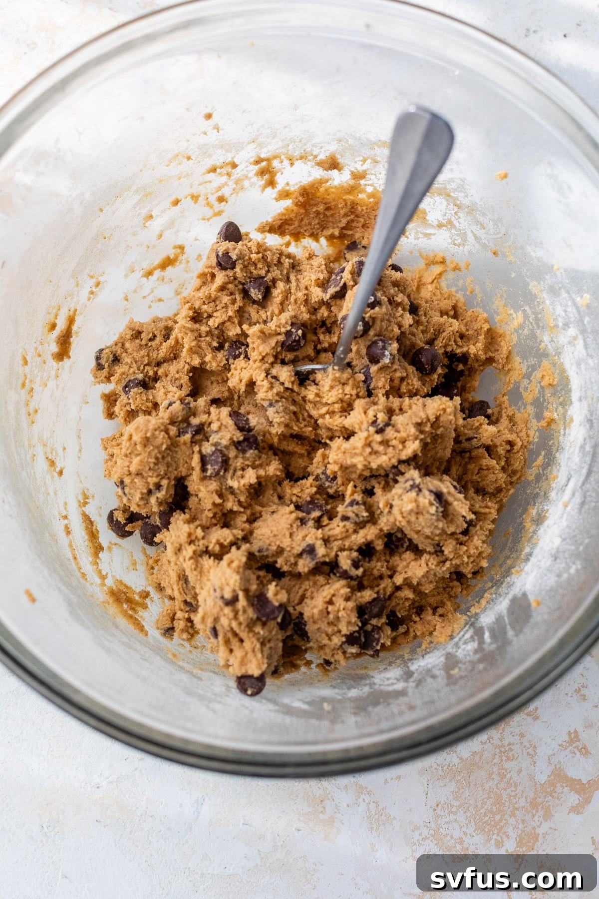 A spoon in a batch of pumpkin chocolate chip cookie dough in a glass bowl.