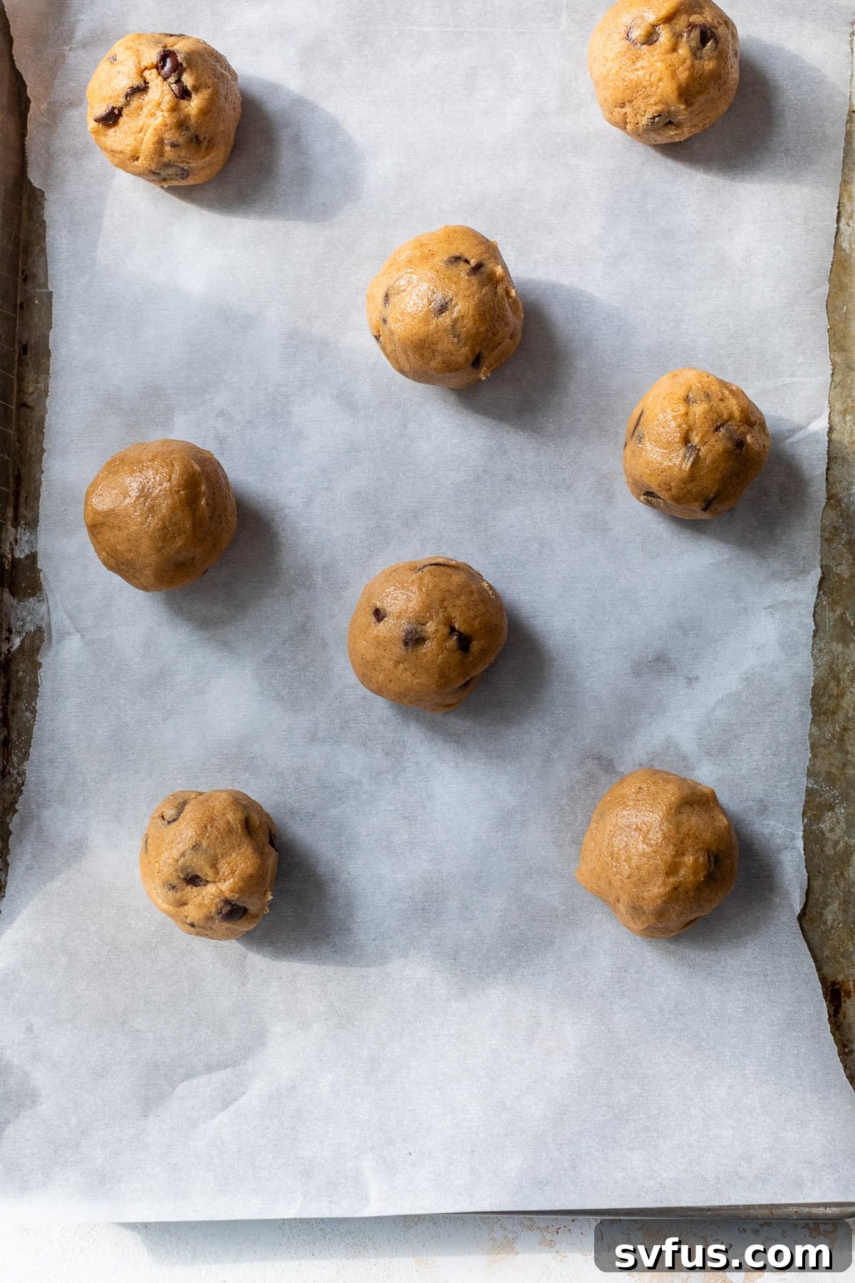 Overhead view of rolled pumpkin chocolate chip cookie dough balls on a parchment-lined baking sheet.
