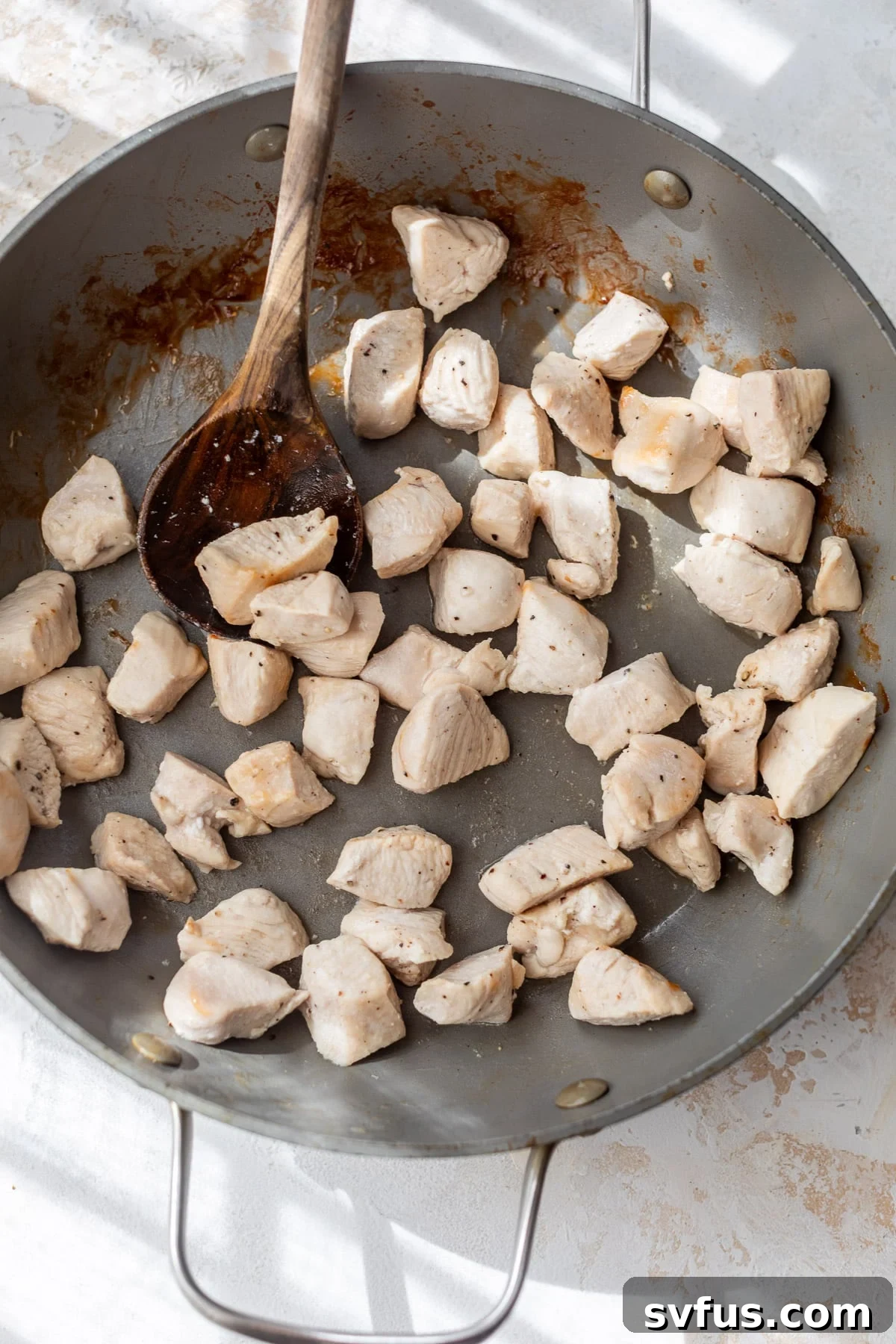 Using a wooden spoon to stir cooked chicken bites in a large skillet, ensuring even searing.