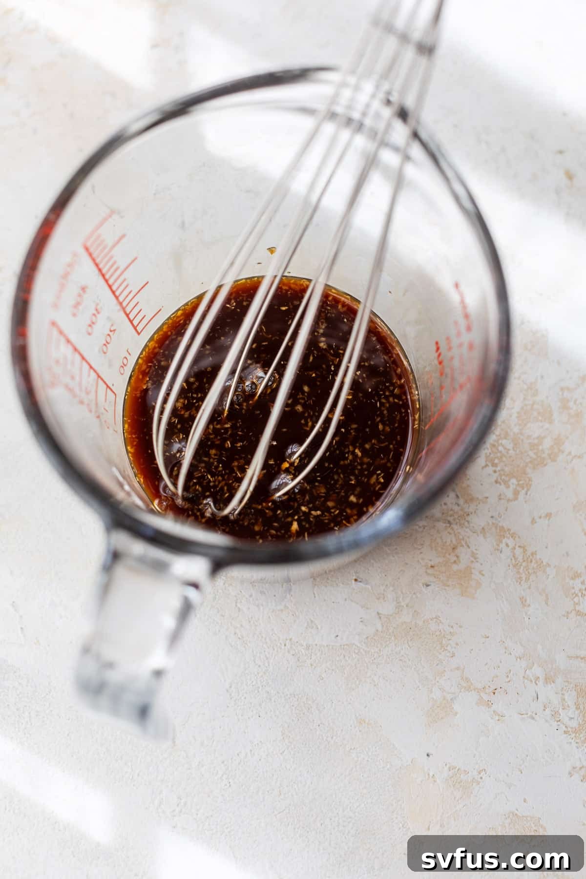 Whisking homemade teriyaki sauce ingredients in a glass measuring cup to ensure smoothness.