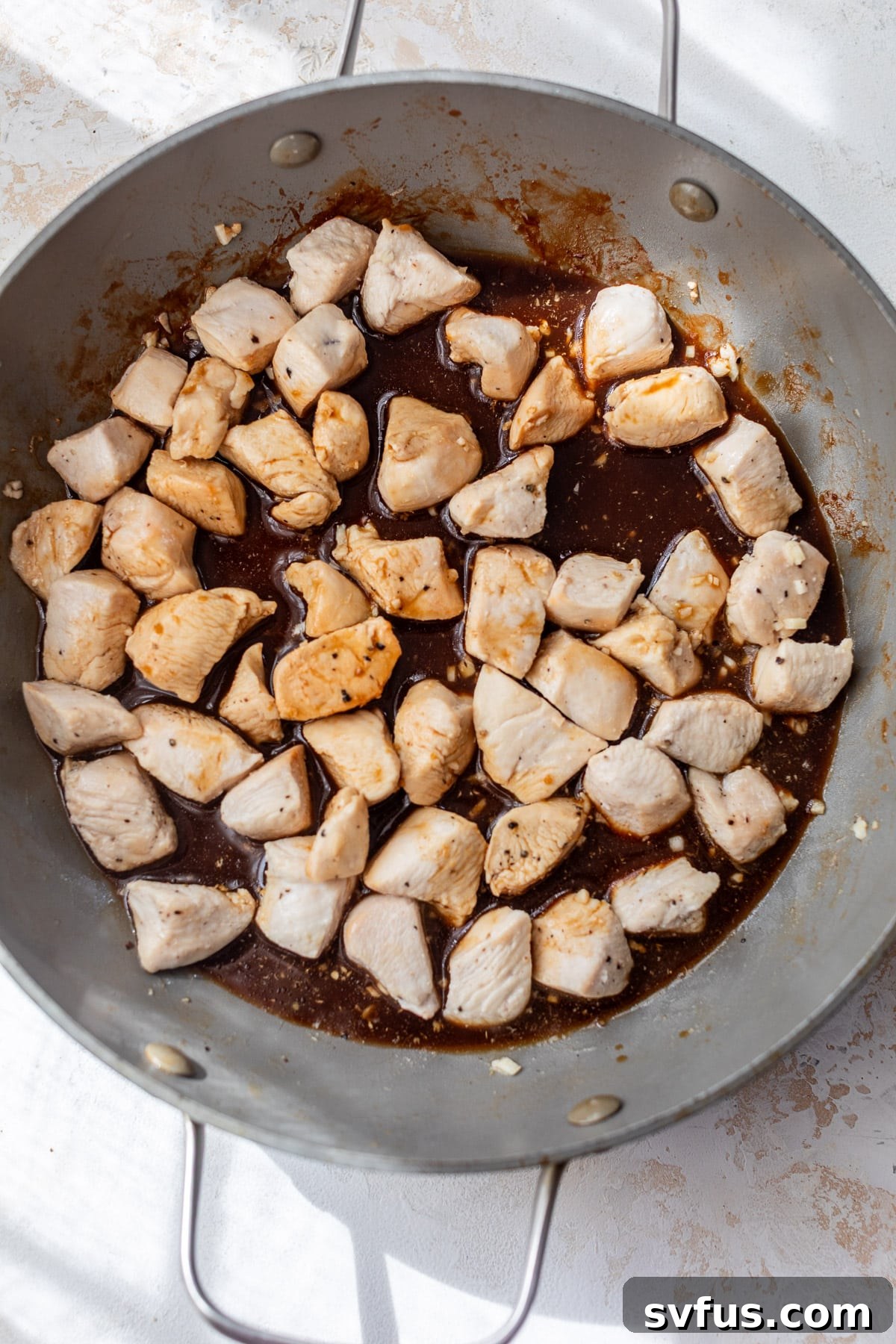 Overhead view of cooked chicken bites covered in glossy teriyaki sauce in a large skillet.