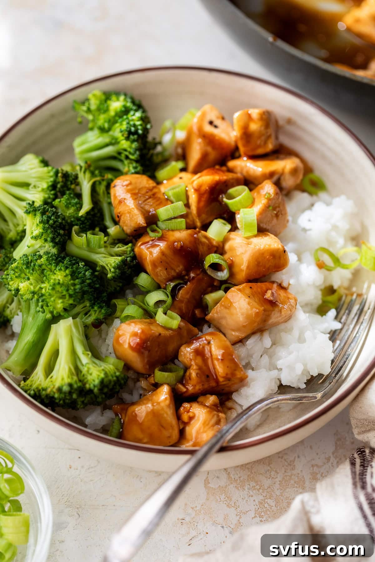 Teriyaki chicken and broccoli served over white rice in a bowl, showing a portion of a delicious meal.