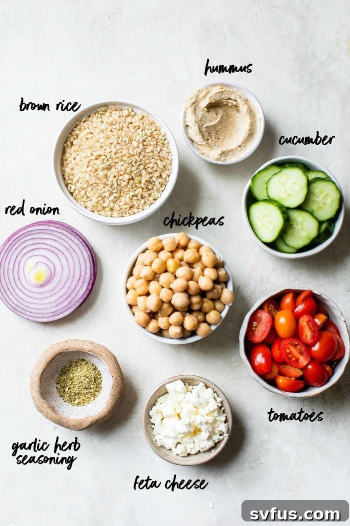 A vibrant display of fresh ingredients for a Mediterranean Hummus Bowl, including brown rice, tomatoes, cucumbers, red onion, feta cheese, chickpeas, and a bowl of hummus.