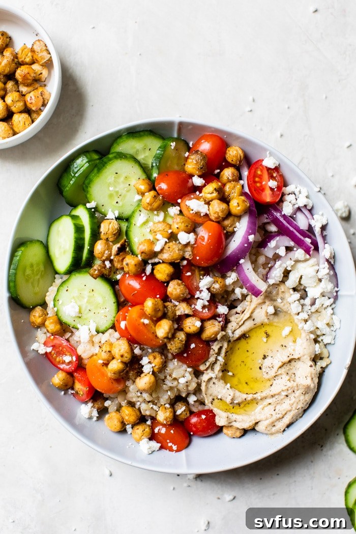 Close-up of a Mediterranean Hummus Bowl showcasing the textures of brown rice, fresh vegetables, crumbled feta cheese, and roasted chickpeas.
