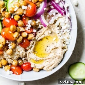 A beautifully presented Mediterranean Hummus Bowl, featuring cooked rice, fresh vegetables, crispy chickpeas, and a dollop of hummus.