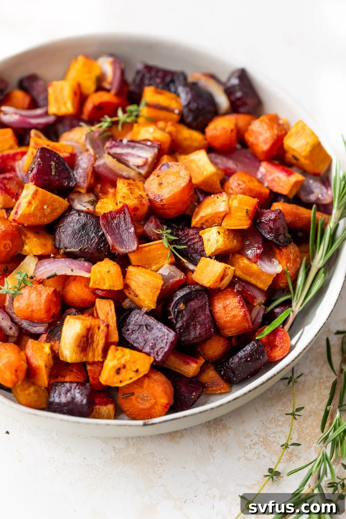 A medley of perfectly roasted root vegetables in a large white serving bowl, showcasing their vibrant colors and crispy edges.