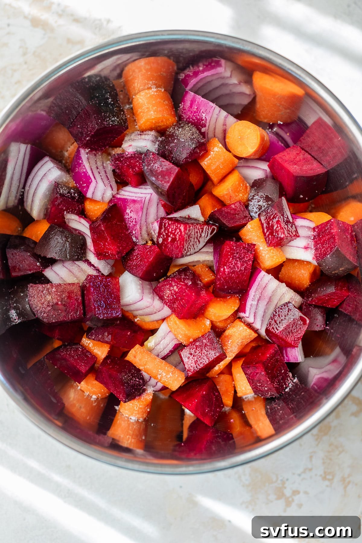 Overhead view of a vibrant medley of raw, chopped root vegetables in a large mixing bowl, perfectly coated with oil and seasoning, ready for roasting.