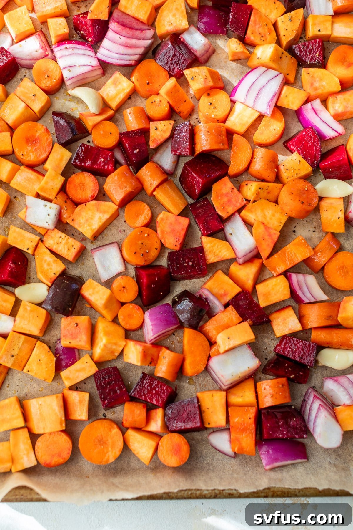 Overhead view of a colorful assortment of raw, chopped root vegetables neatly arranged in a single layer on a parchment-lined sheet pan, ready for the oven.