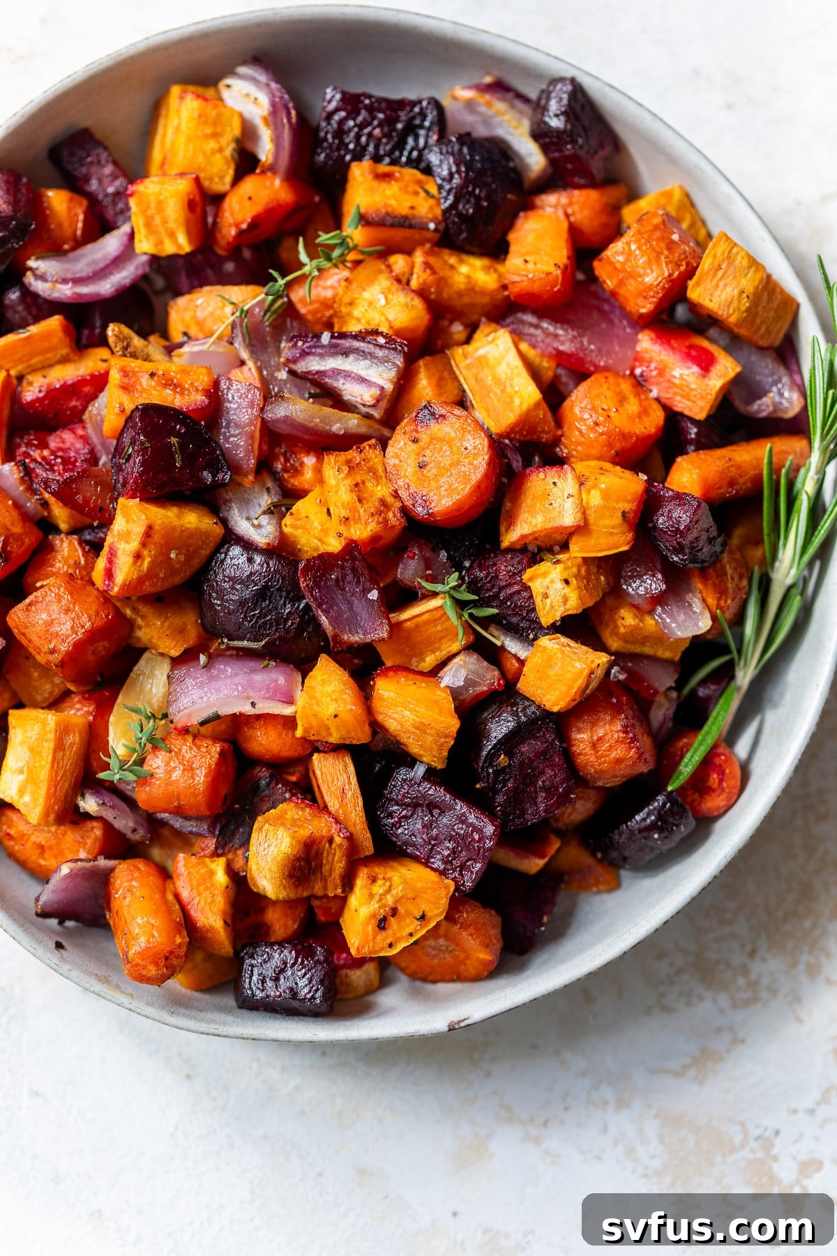 A large white bowl filled with a colorful medley of roasted root vegetables, garnished with fresh herbs, ready for serving.