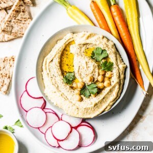 A bowl of hummus topped with chickpeas surrounded by vegetables and pita bread.