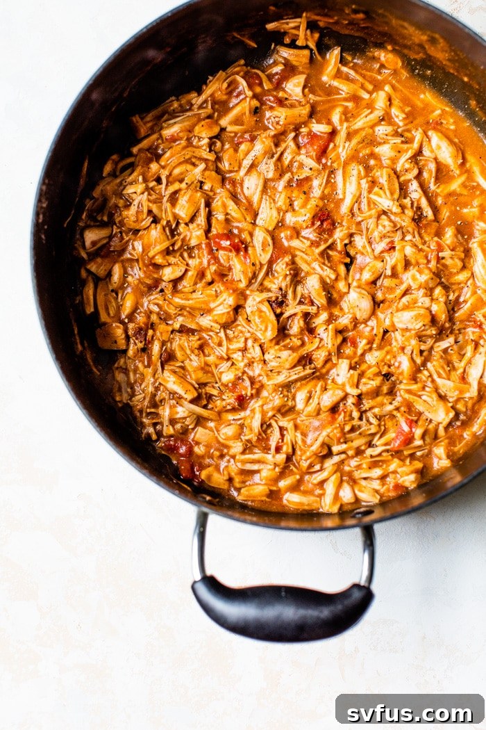 A cast-iron skillet filled with shredded jackfruit simmering in a rich barbecue sauce, mixed with fire-roasted tomatoes and aromatic spices, ready to absorb all the delicious flavors.