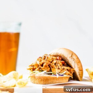 A hamburger bun filled with pulled jackfruit served with chips and beer, depicting the delicious outcome of the recipe.