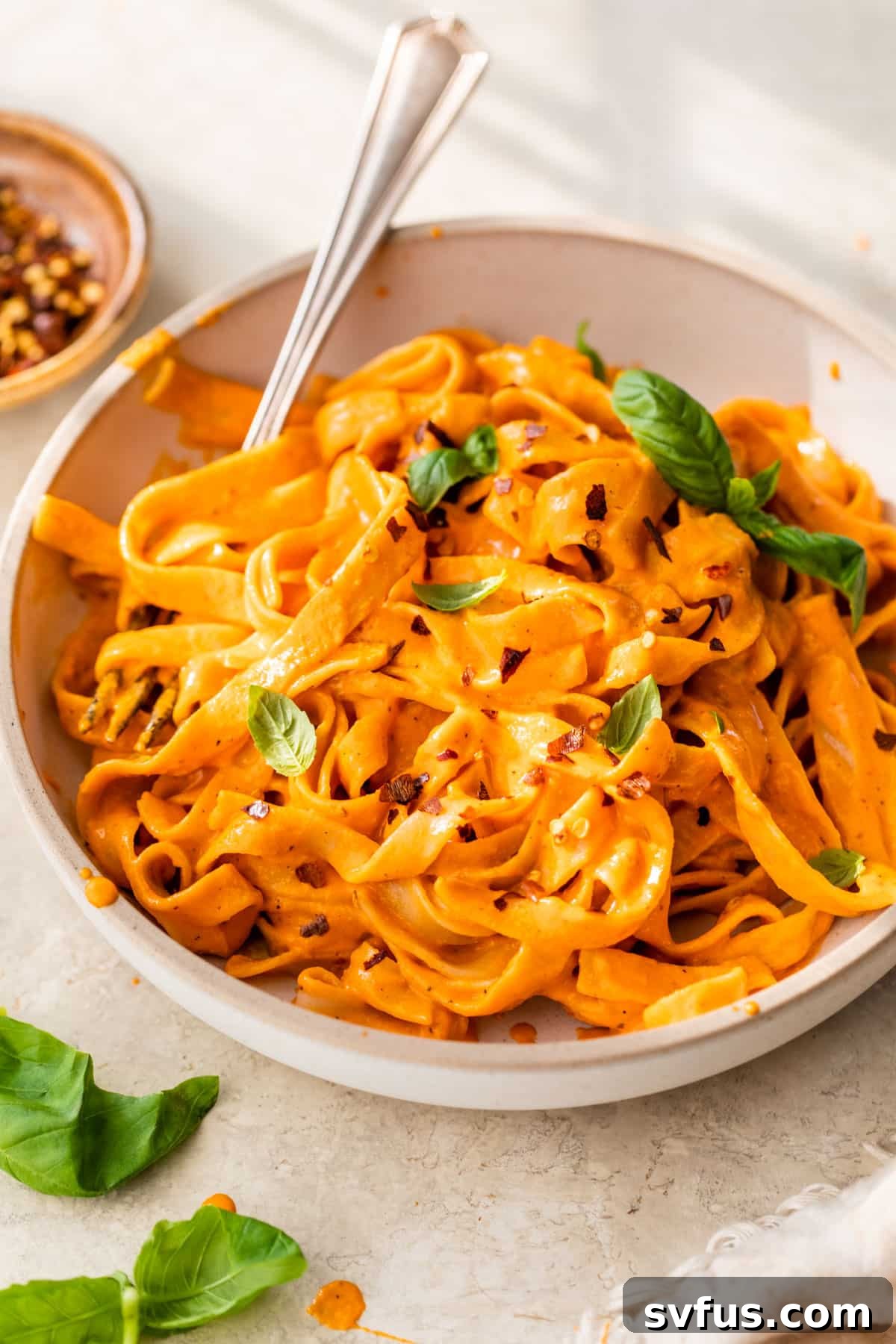 A large ceramic bowl filled with creamy vegan roasted red pepper pasta, adorned with fresh basil leaves, ready to be served.