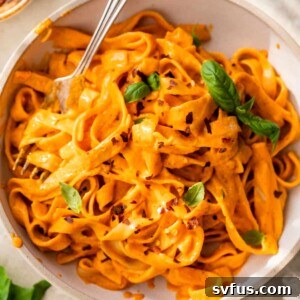 A bowl of long pasta with a fork twirled around it, topped with fresh basil