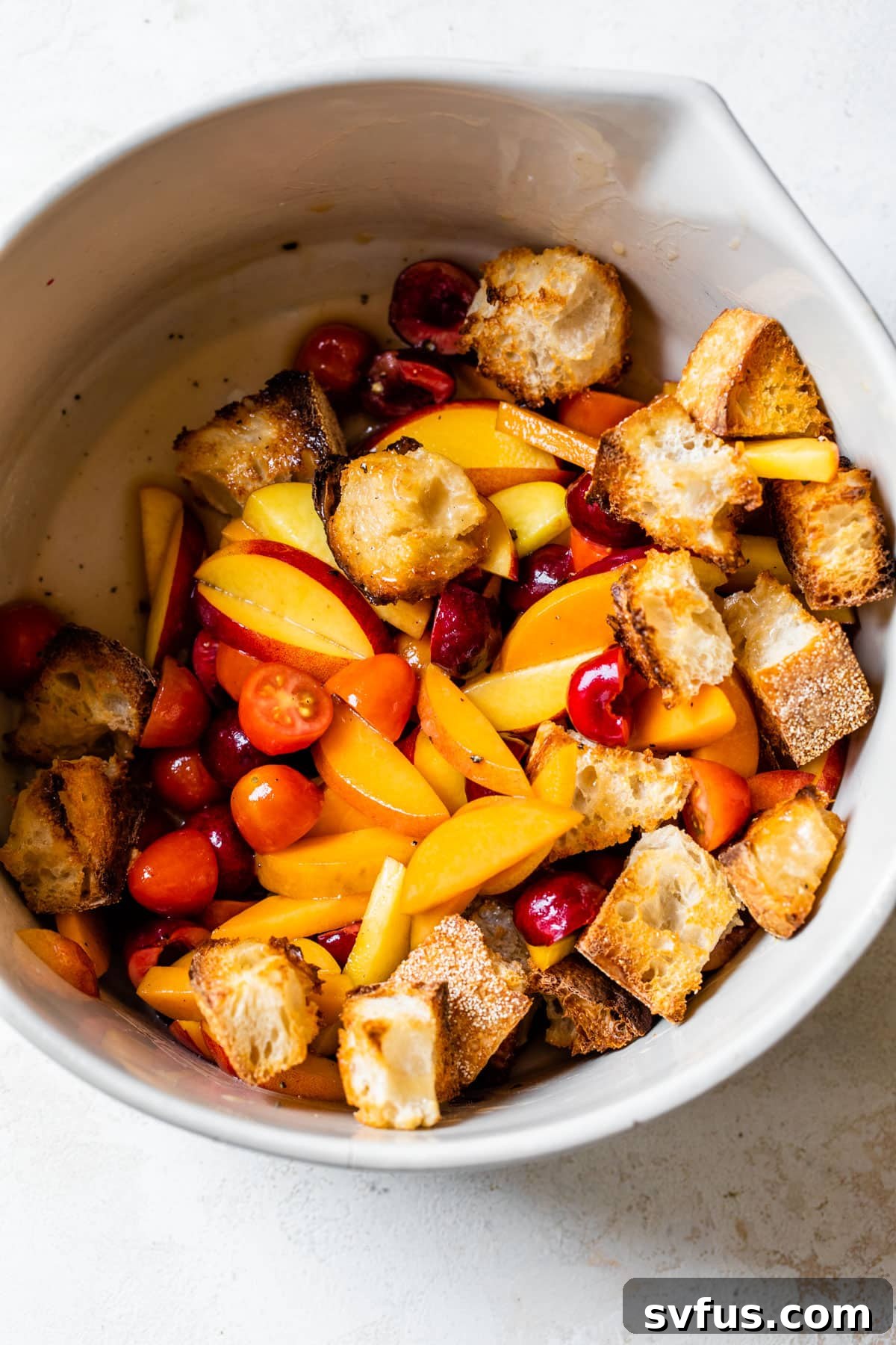 A large bowl generously filled with a Stone Fruit Panzanella Salad, featuring juicy peaches, vibrant cherries, ripe tomatoes, and golden toasted bread cubes.