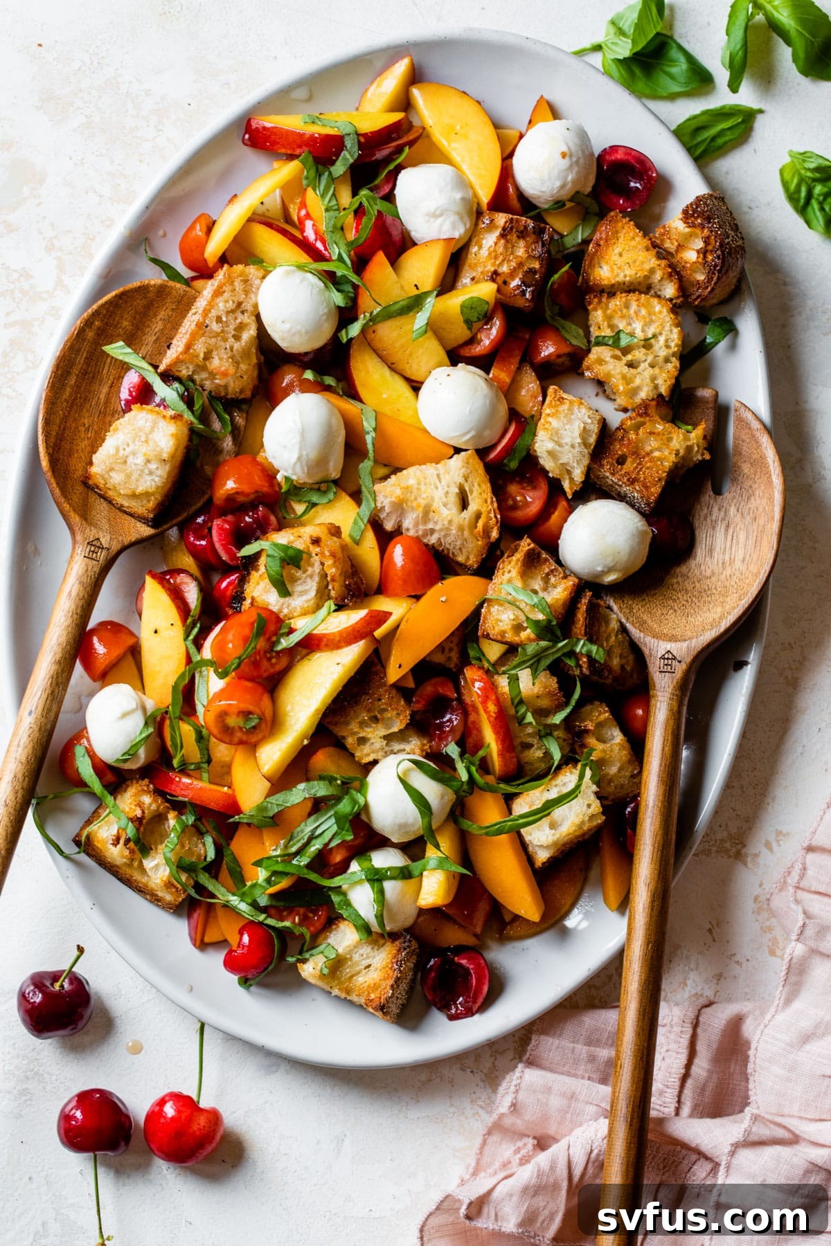 A vibrant Stone Fruit Panzanella Salad presented on a white serving platter, ready to be enjoyed, with wooden serving spoons visible.