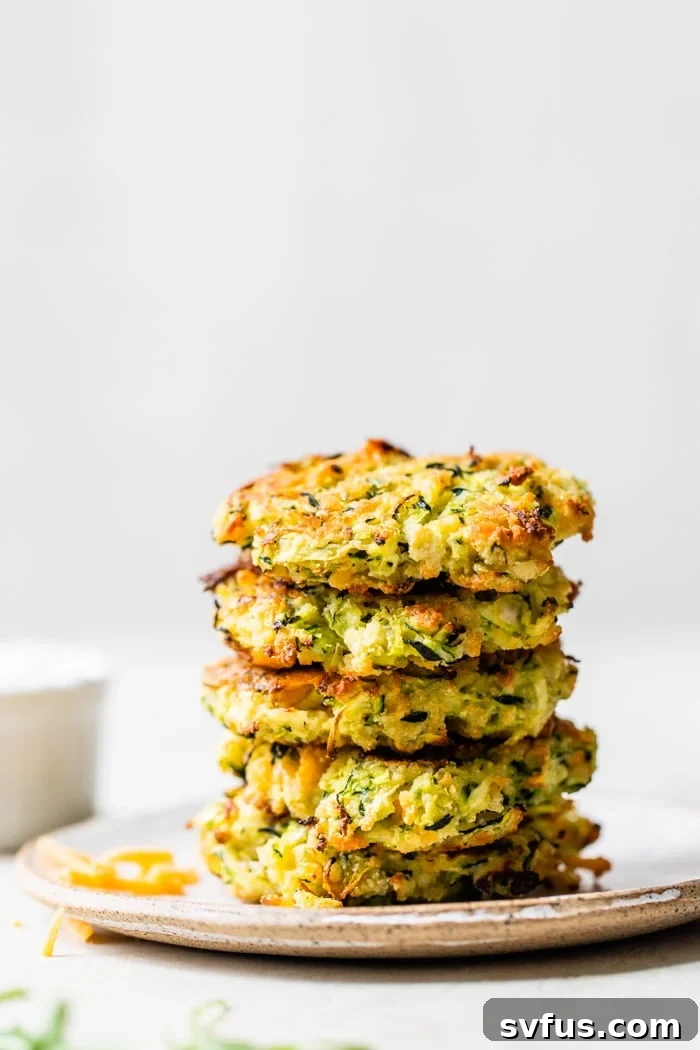 a stack of crispy golden-brown zucchini fritters on a white plate, garnished with fresh herbs