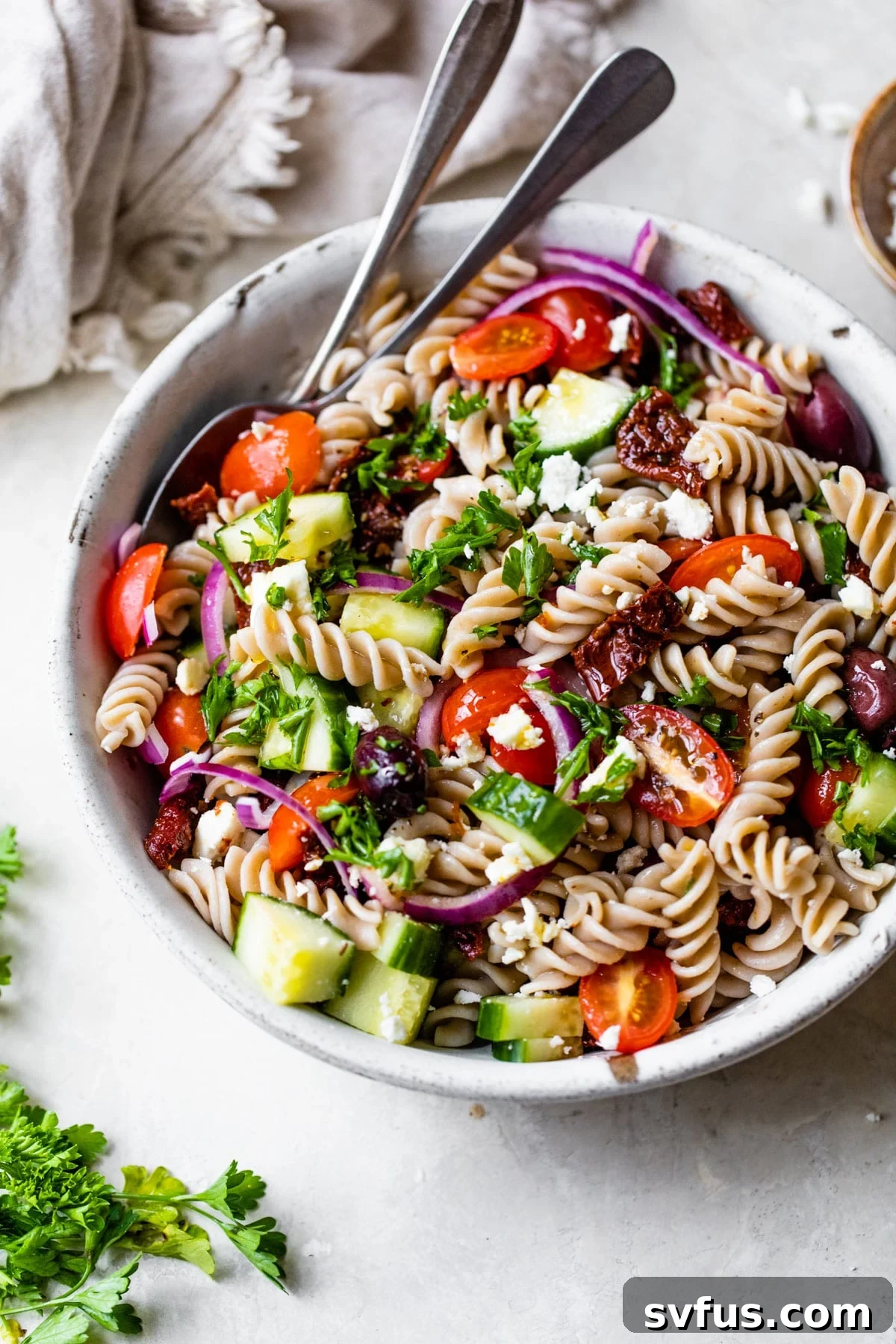 Close-up of Mediterranean Pasta Salad in a bowl, showcasing fresh tomatoes, red onion, and crumbled feta cheese