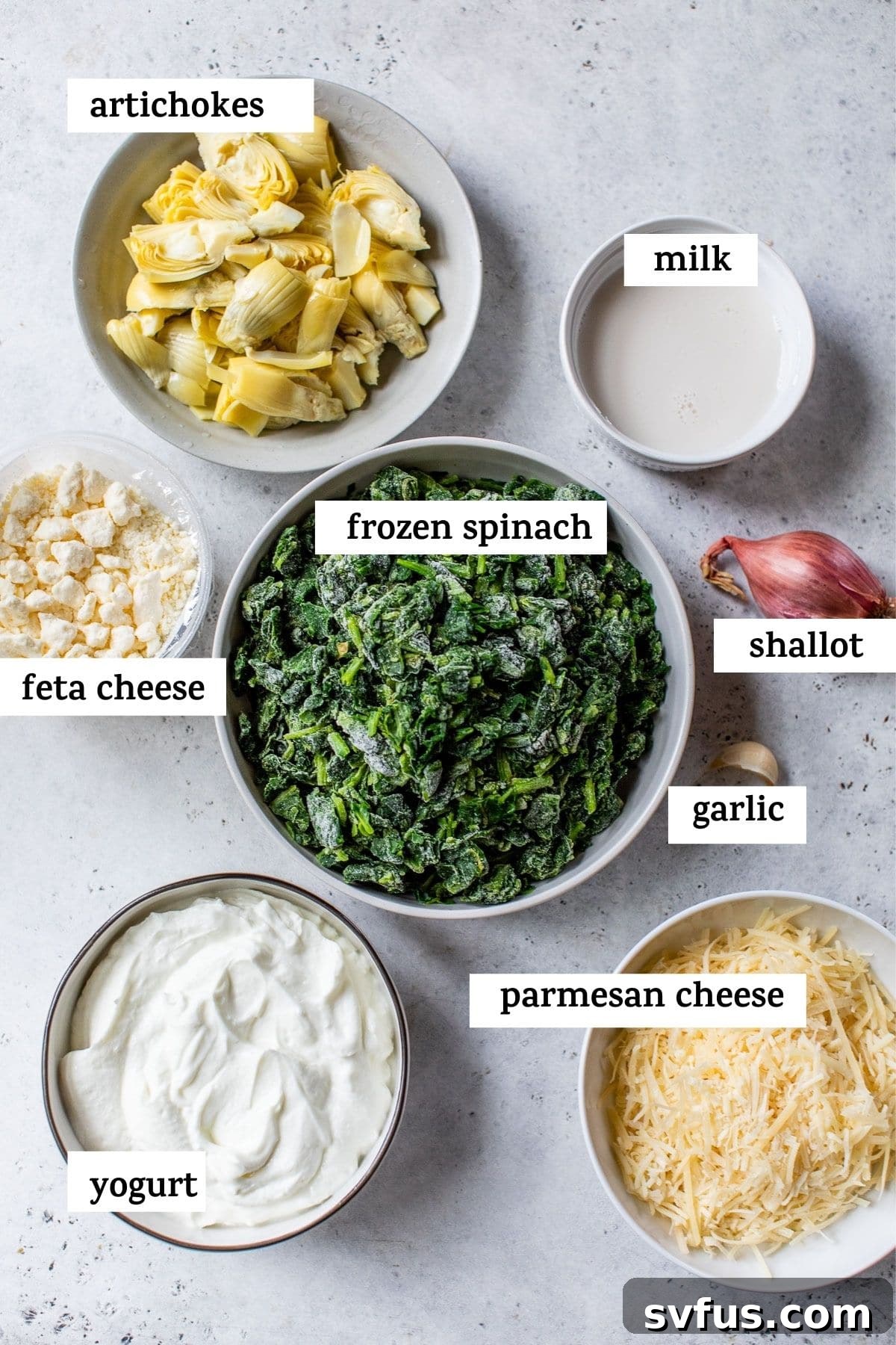 All the fresh ingredients for Crockpot Spinach Artichoke Dip laid out on a clean surface, including spinach, artichokes, cheeses, and Greek yogurt.