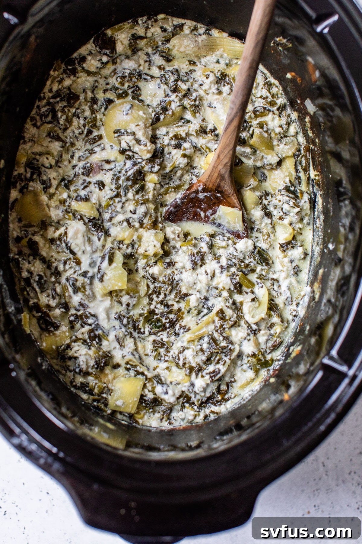 A close-up shot of the finished creamy spinach artichoke dip, hot and bubbling in the crockpot, ready to be served.