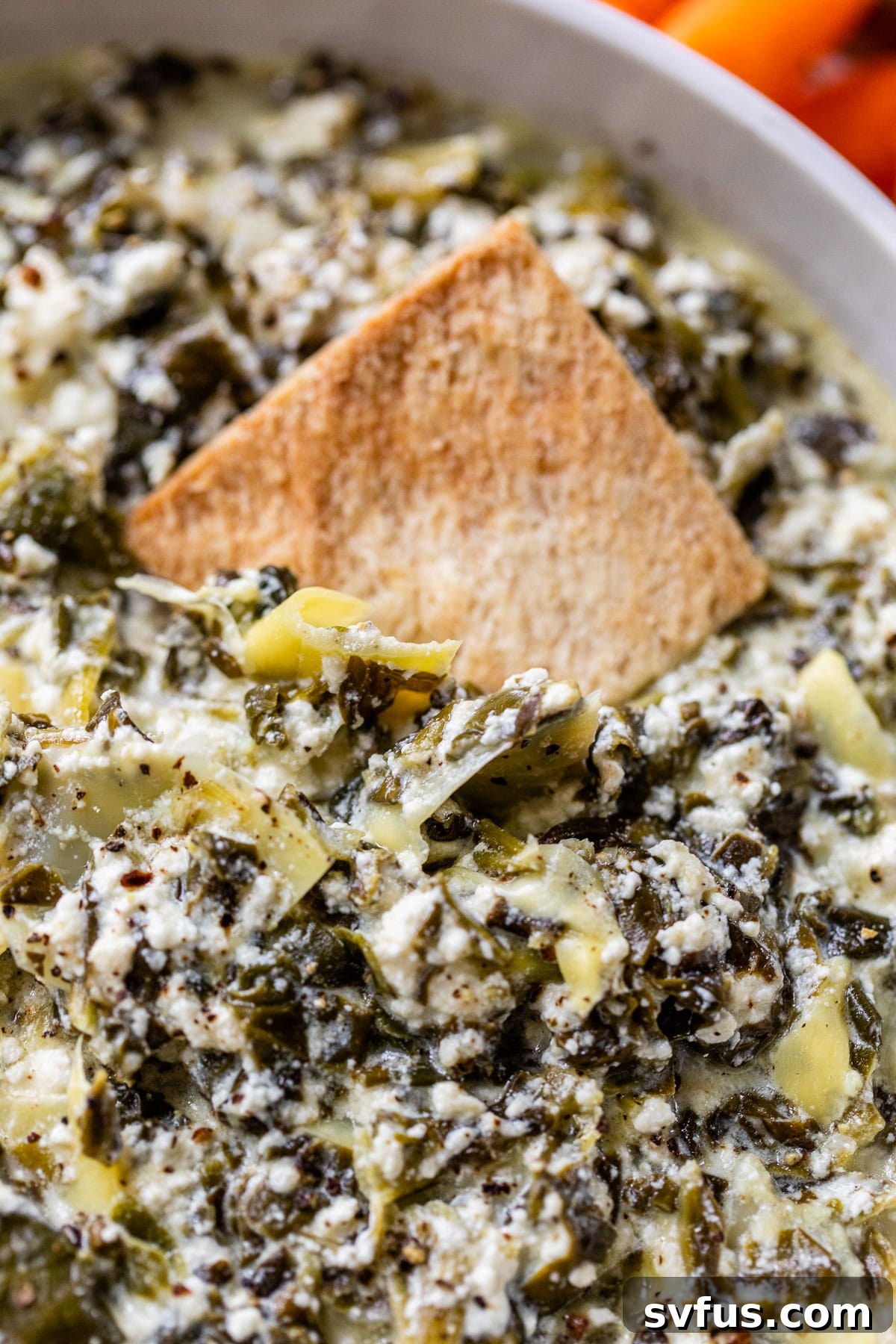 A pita chip gracefully scooping a generous portion of creamy spinach artichoke dip, showcasing its rich texture.