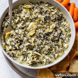 A bowl of dip beside pita chips and baby carrots