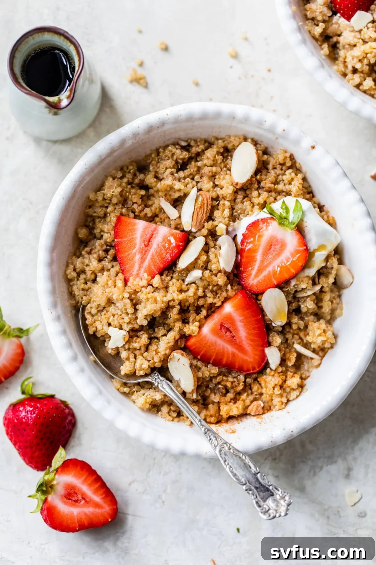 A vibrant Quinoa Breakfast Bowl with sliced strawberries and almonds, placed next to a small dish of golden maple syrup, emphasizing its wholesome appeal.