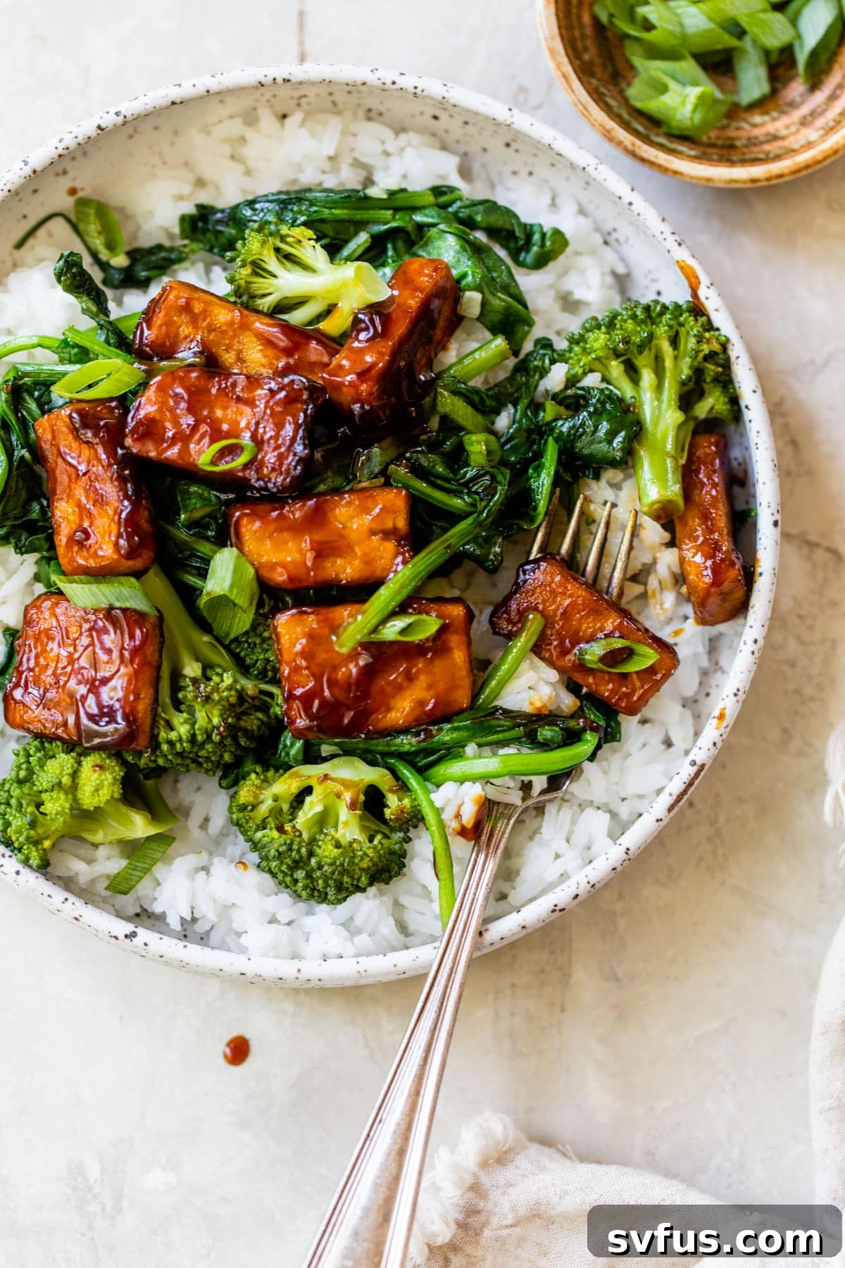A vibrant bowl of Teriyaki Tofu Stir Fry, showcasing the crispy golden tofu, fresh green broccoli, and tender wilted spinach artfully arranged over a bed of fluffy white rice, garnished with finely chopped green onions, ready for a healthy meal.