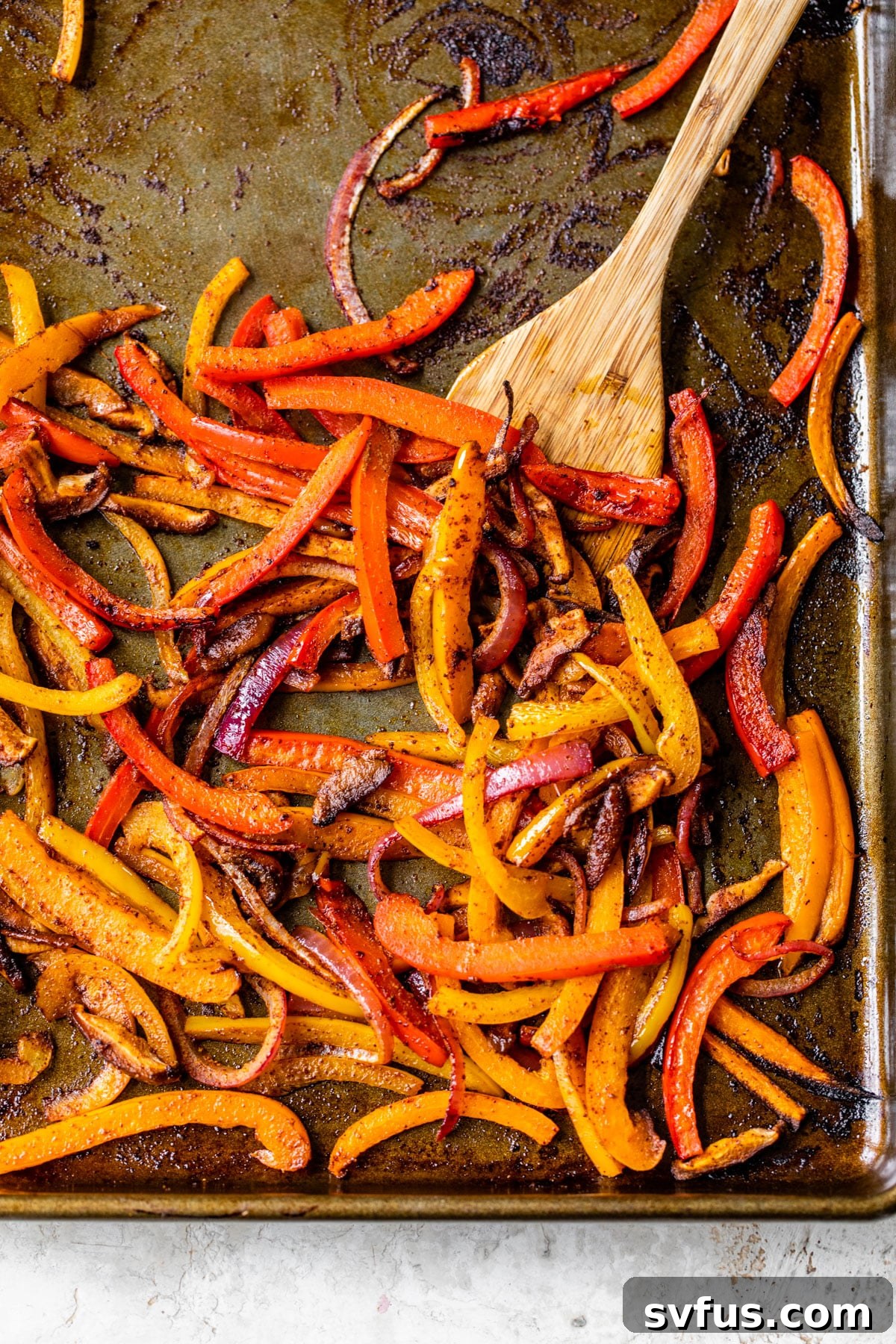 Close-up of cooked bell peppers, red onion, and mushrooms perfectly roasted on a baking sheet, ready for fajita assembly.