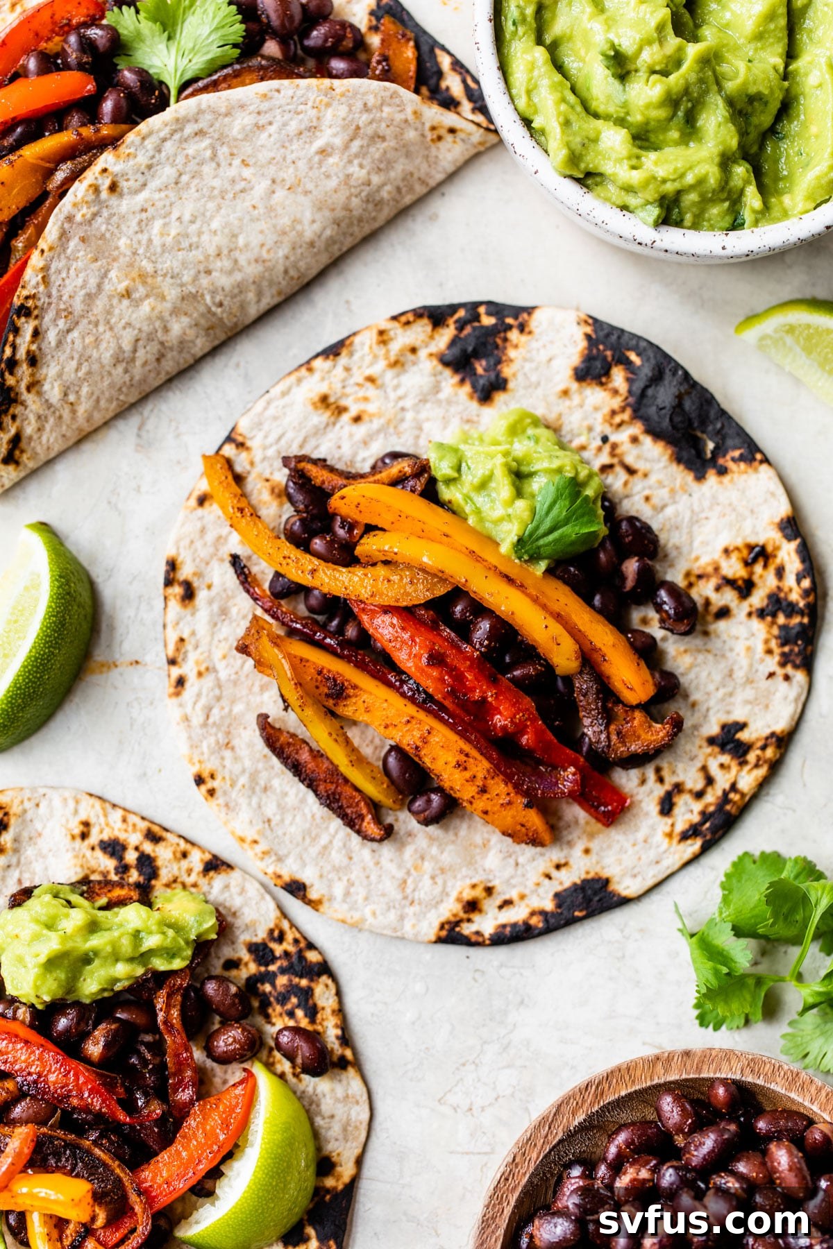 Two fully assembled vegetarian fajitas with colorful peppers, black beans, and guacamole, garnished with cilantro.