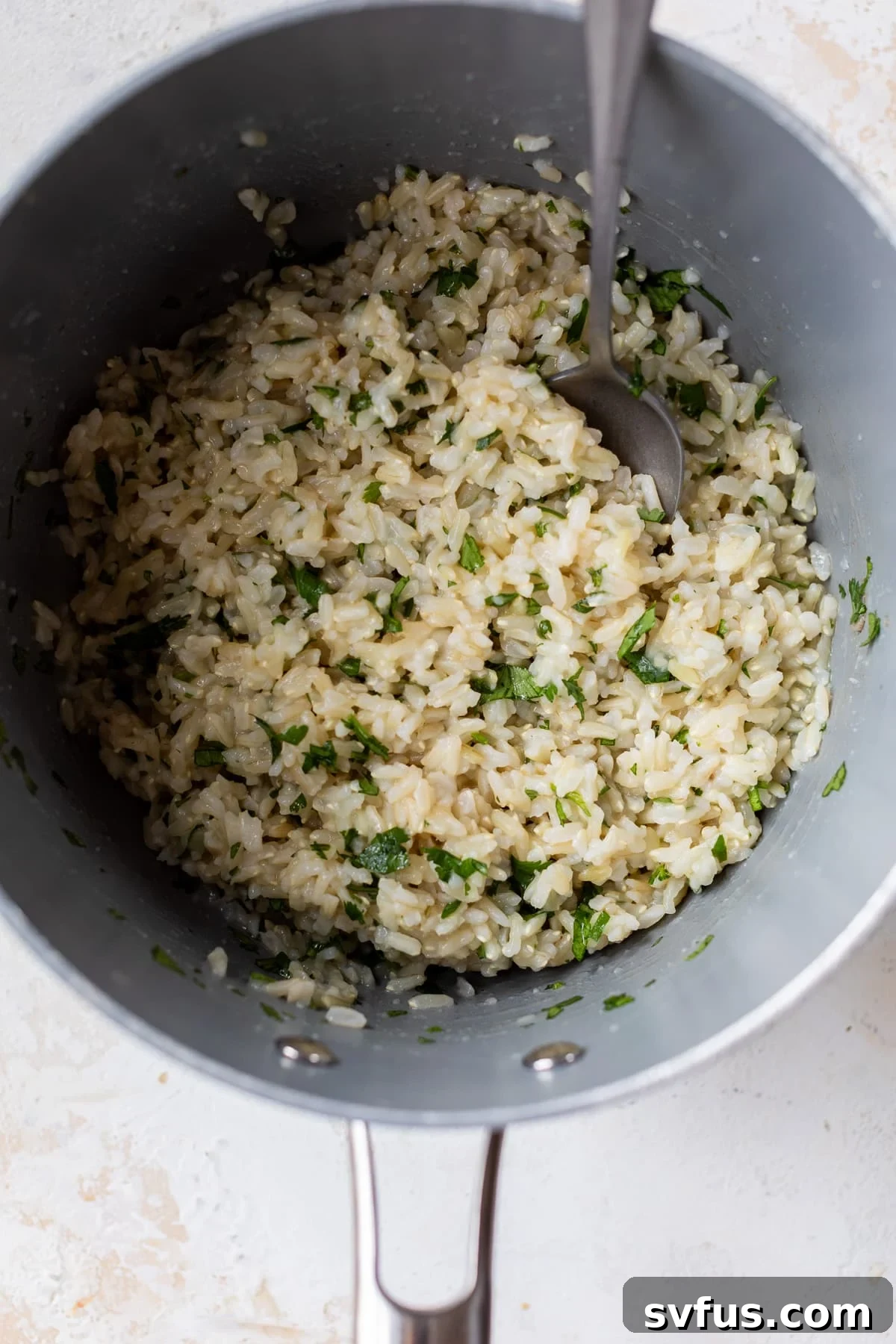 Cilantro Lime Brown Rice being stirred in a pot with a spoon, showing the green flecks of cilantro mixed throughout.