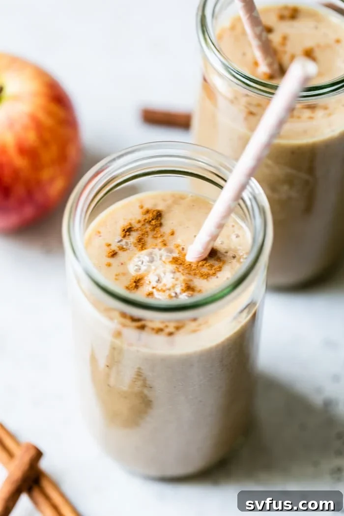 A freshly poured apple smoothie in a glass, topped with an apple slice and cinnamon, showcasing its smooth, appealing texture.