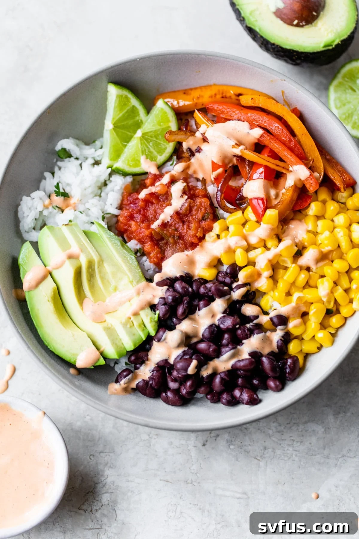 A vibrant bowl of cilantro-lime rice topped with black beans, corn, colorful bell peppers, creamy avocado slices, zesty salsa, and a drizzle of chipotle aioli, ready to be enjoyed.