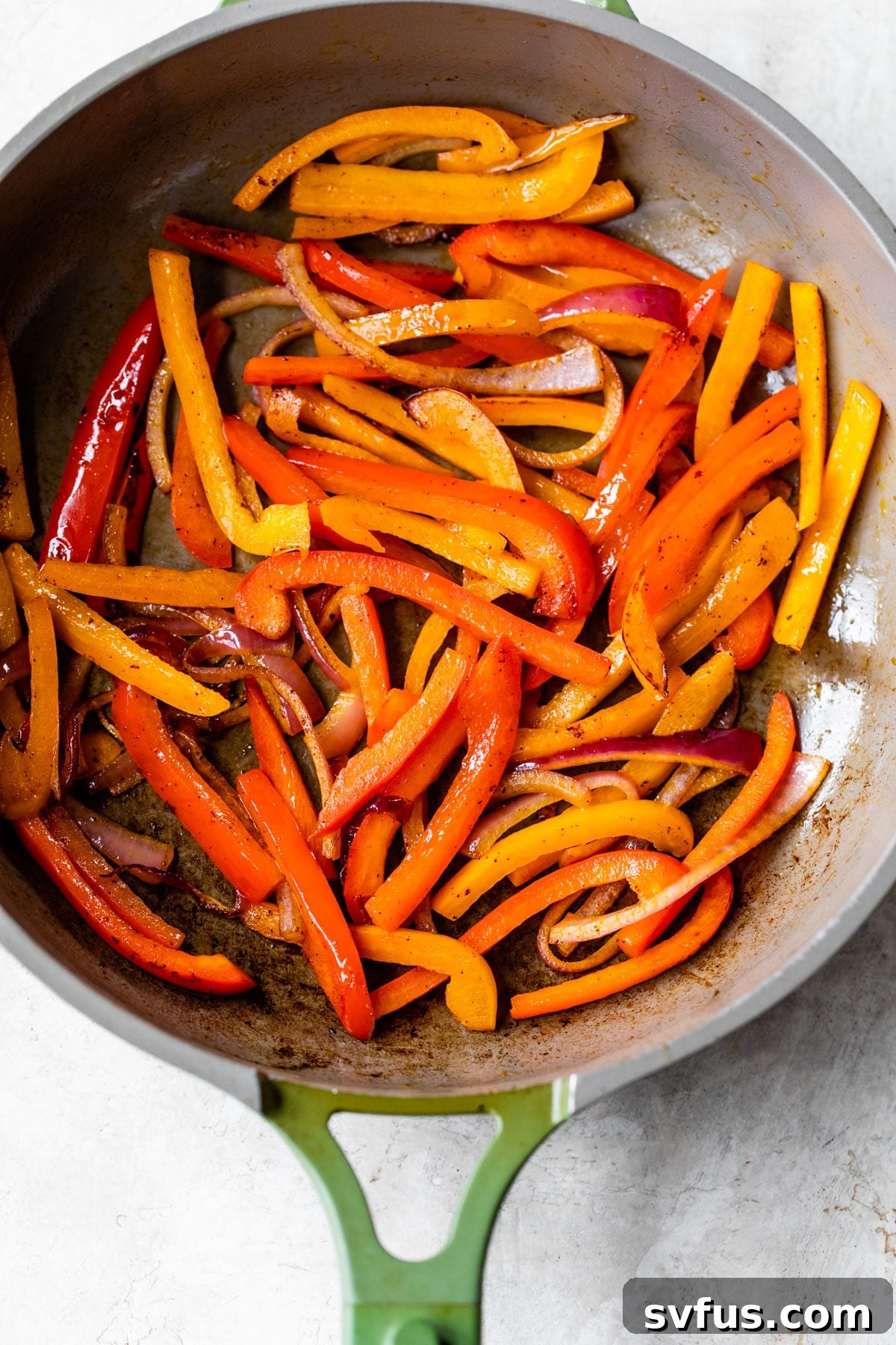 Sliced bell peppers and red onion sizzling in a skillet, seasoned with chipotle spice, creating aromatic fajita vegetables for the burrito bowl.